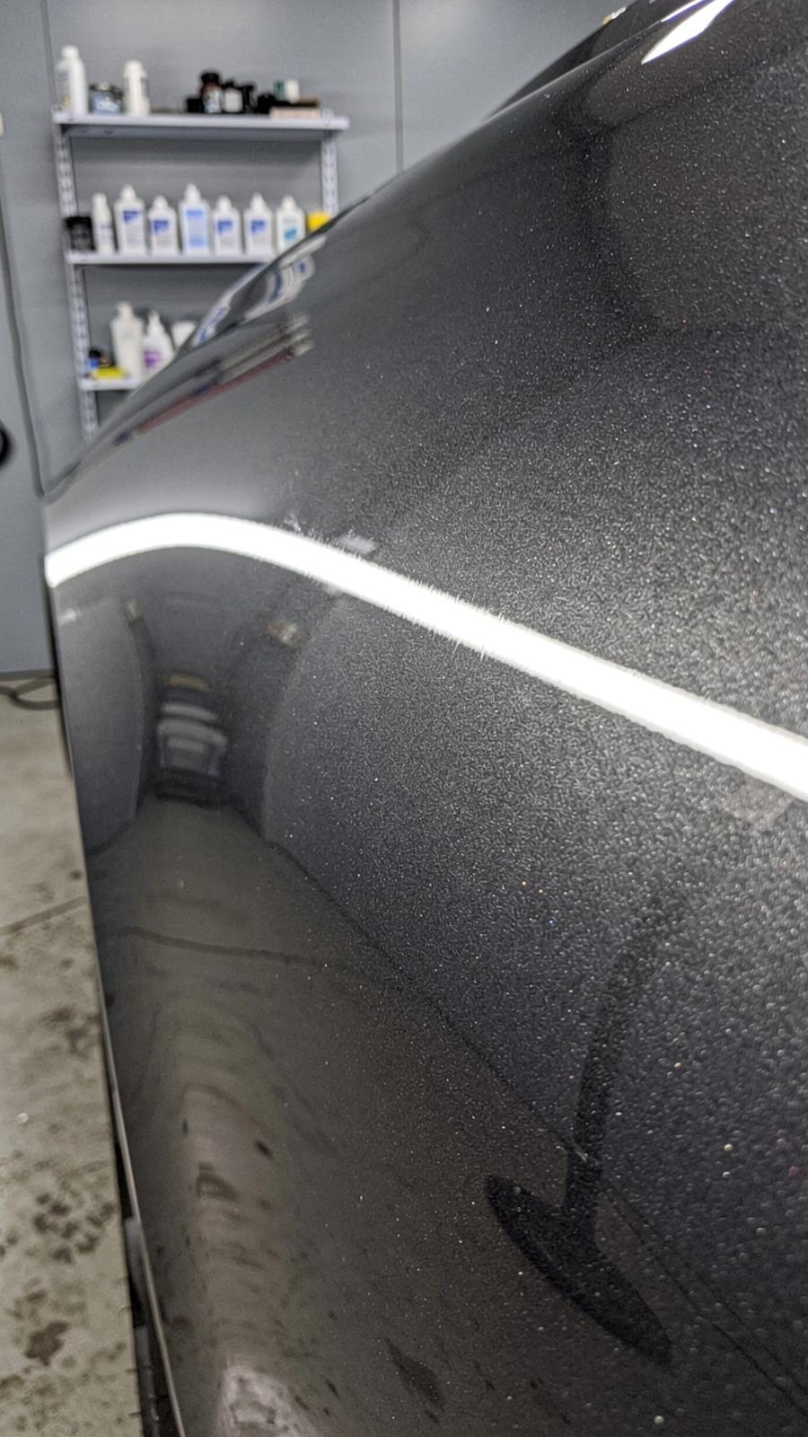Macro view of a dark grey car panel under studio light showing the edge of an installed paint protection film